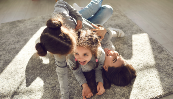 Happy-family-enjoying-quality-time-at-home.-Mom-and-little-children-frolicking-on-carpet